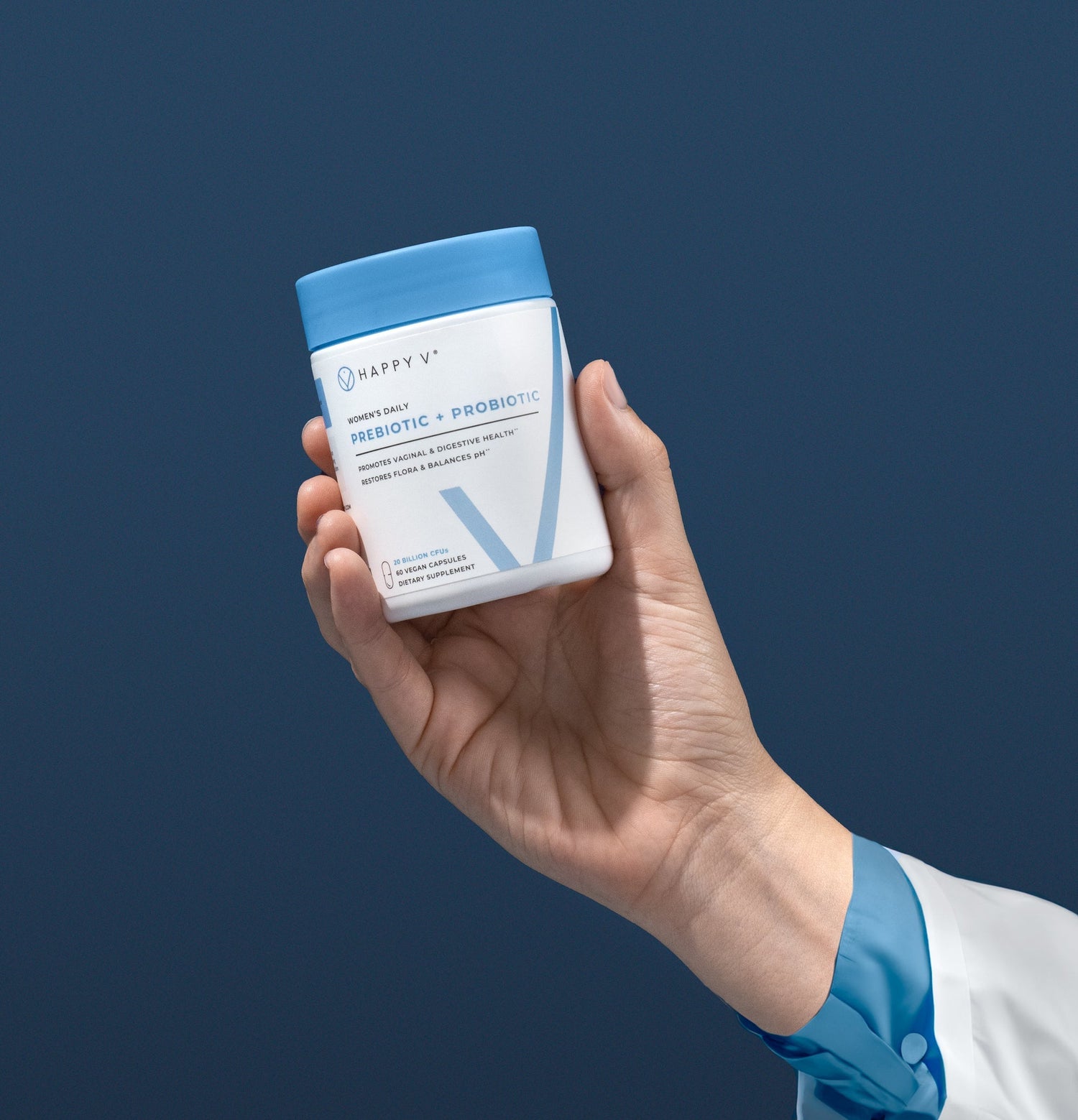 Happy V prebiotic and probiotic bottle held in a hand against a blue background.