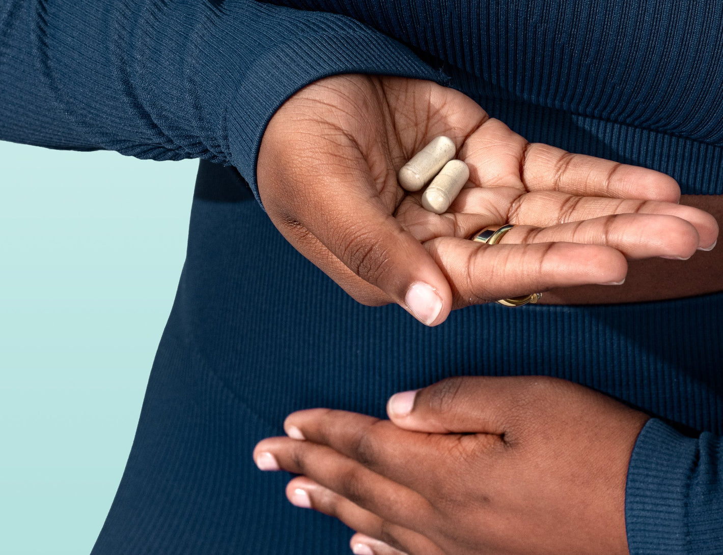 Hands holding two Happy V supplement capsules against a light background, promoting feminine wellness.